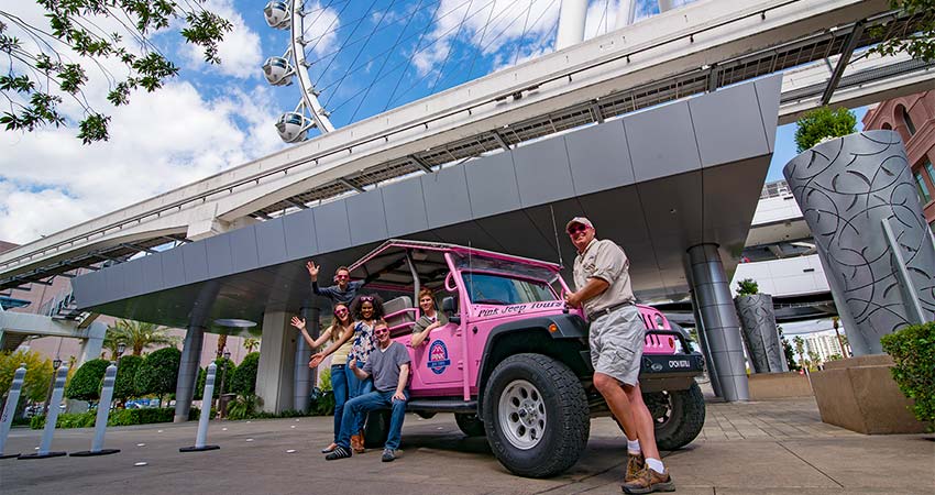 Pink Jeep Tours Adventure guide and tour guests striking a photo pos on a Pink Jeep Wrangler with the Las Vegas High Roller in the background.