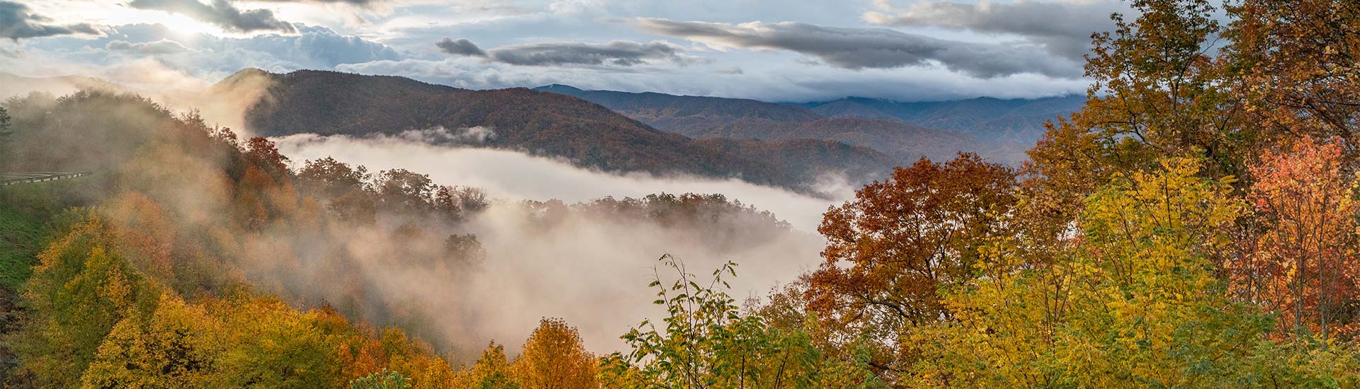 Panoramic view the Great Smoky Mountains National Park hilltops exploding with vibrant fall foliage and low-hanging clouds.