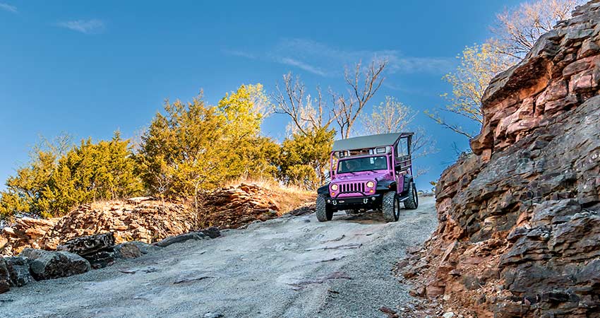 Pink Jeep Wrangler on a steep rocky descent down Baird Mountain with fall foliage, Pink Jeep Tours Branson.