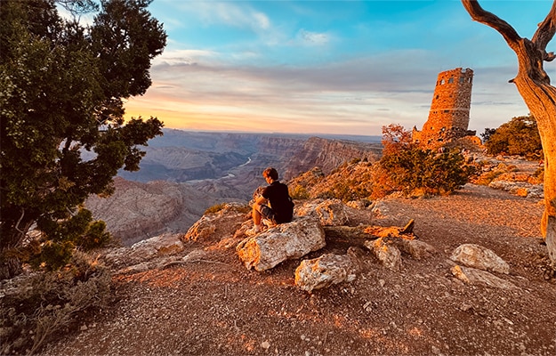 A traveler enjoys a breathtaking Grand Canyon sunset near Desert View Watchtower, surrounded by golden canyon views.