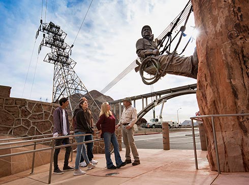 Group of tour guests with guide looking at the bronze High Scaler Monument at Hoover Dam, Pink Jeep Las Vegas to Hoover Dam tour.