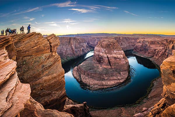 Visitors overlook Horseshoe Bend near Page, Arizona, where the Colorado River curves around towering sandstone cliffs beneath a clear evening sky.