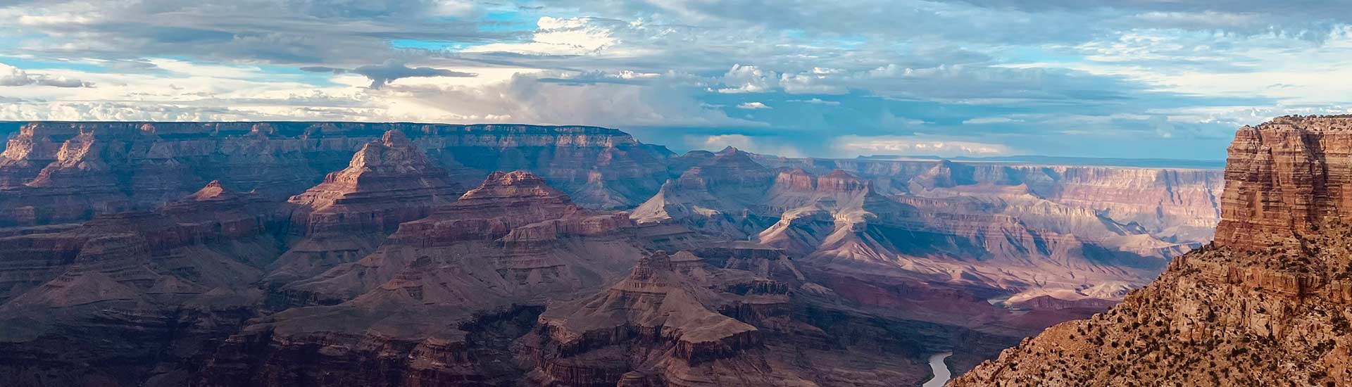 Beautiful view of the Grand Canyon's layered ridges with the Colorado River winding below, under a teal blue sky with clouds above.