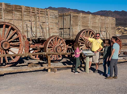 Pink Adventure Death Valley Tour guide and guests talking next to Twenty-Mule Team Wagon at Harmony Borax Works