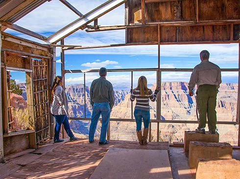 Four people standing in a building looking out floor-to-ceiling windows overlooking the Grand Canyon West Rim, Pink Jeep Tours.