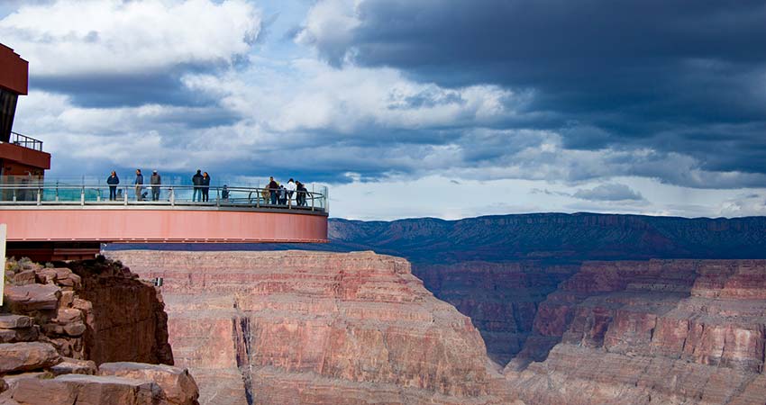 People standing atop the Grand Canyon Skywalk overlooking the Grand Canyon West Rim at Eagle Point, with storm clouds above.